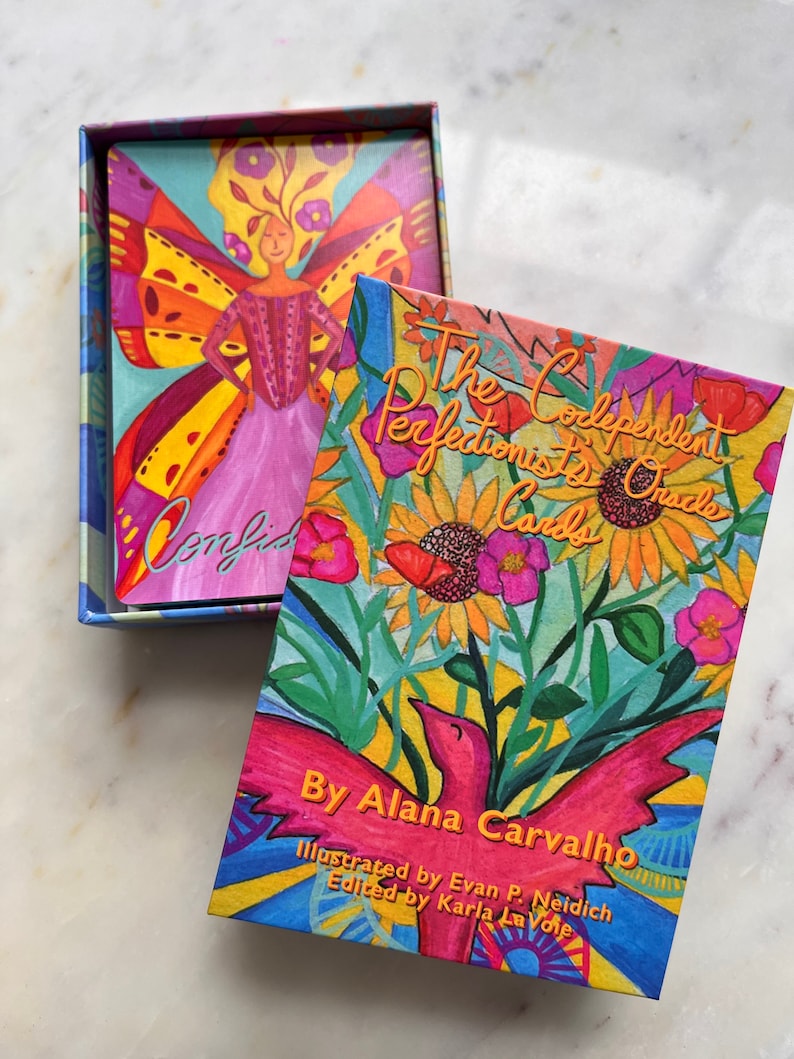 May include: A box of The Codependent Perfectionist's Oracle Cards by Alana Carvalho. The box features a colorful illustration of flowers and a bird with a bright pink body. The text on the box reads "The Codependent Perfectionist's Oracle Cards" and "By Alana Carvalho".