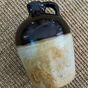 May include: A brown and white glazed ceramic jug with a handle. The jug has a rounded body and a narrow neck.