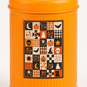 May include: A cylindrical orange metal canister with a silver handle on the lid. The front features a rectangular patch-style graphic with a grid of Halloween-themed icons including pumpkins, ghosts, skulls, bats, cats, stars, and moons.