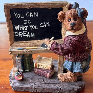 May include: A brown bear figurine wearing a blue bow and a red sweater, standing next to a chalkboard. The chalkboard reads "You CAN DO WHAT YOU CAN DREAM". Books labeled "Math" and "Science" are at the base.
