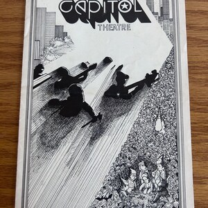 May include: Black and white vintage theater program cover. The cover features the text "CAPITOL THEATRE" with an illustration of figures and a cityscape. The program is presented by John Scher.