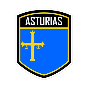 May include: A blue and yellow shield-shaped sticker with the word "ASTURIAS" in black text at the top and a gold cross with a bell and a ring on a blue background.