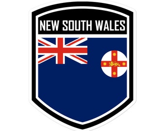 May include: A blue and white shield-shaped sticker with a black border. The sticker features the flag of New South Wales, Australia, with the text "NEW SOUTH WALES" at the top.