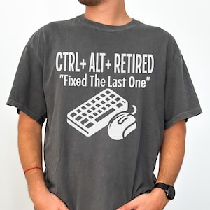 May include: Dark gray t-shirt with the text "CTRL + ALT + RETIRED" and "Fixed The Last One" in white. A white keyboard and mouse graphic are below the text. The shirt is a casual style.