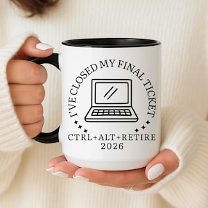 May include: White ceramic mug with a black handle and rim. The mug features the text "I'VE CLOSED MY FINAL TICKET" around a laptop graphic, with "CTRL+ALT+RETIRE 2026" below. The mug is held by a person.