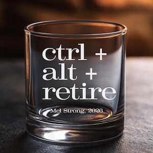 May include: A clear glass tumbler with the words "ctrl + alt + retire" in white, along with "Mel Strong, 2026". The glass is cylindrical and appears to be empty, with a dark background.