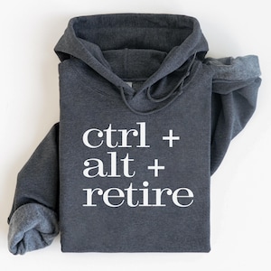 May include: Dark gray hoodie with the text "ctrl + alt + retire" in white. The hoodie has a drawstring hood and long sleeves. The text is centered on the front of the folded garment.
