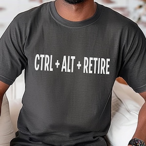 May include: A dark gray t-shirt with the text "CTRL + ALT + RETIRE" printed in white.