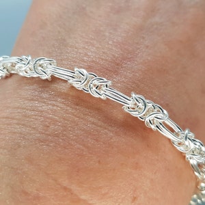 Peut inclure: Un bracelet en argent avec un motif de chaîne tissée. Le bracelet est porté au poignet.