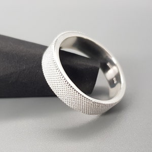 Op de afbeelding: Een zilveren ring met een getextureerd oppervlak. De ring is dik en heeft een afgeronde vorm.