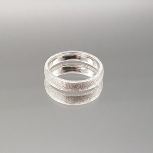 Può includere: Un anello a fascia d'argento con una superficie testurizzata.