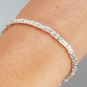 Peut inclure: Un bracelet en argent avec un motif byzantin. Le bracelet est porté au poignet.