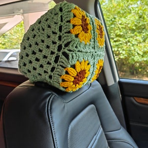 Puede incluir: Reposacabezas de ganchillo verde con dise&ntilde;os de girasoles. El reposacabezas est&aacute; en un asiento de coche.