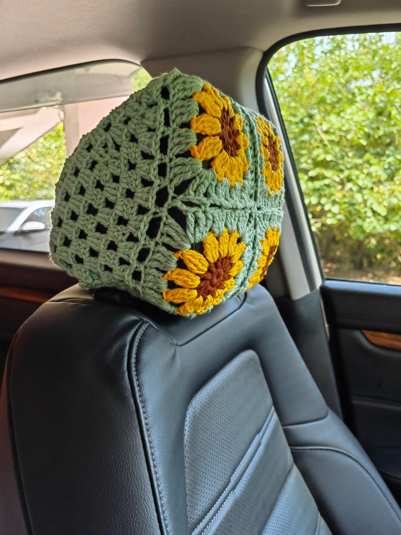 Puede incluir: Reposacabezas de ganchillo verde con dise&ntilde;os de girasoles. El reposacabezas est&aacute; en un asiento de coche.