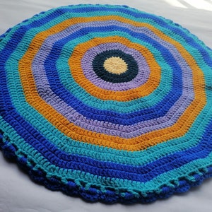 May include: A round crocheted rug with a multi-colored concentric circle pattern. The rug is made with blue, teal, purple, and orange yarn.