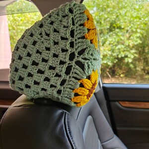 Puede incluir: Un reposacabezas de asiento de coche de ganchillo con un dise&ntilde;o de girasol verde y amarillo. El reposacabezas est&aacute; hecho de un hilo suave y texturizado y est&aacute; dise&ntilde;ado para agregar un toque de comodidad y estilo a cualquier coche.