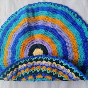 May include: A colorful crocheted round rug with a multi-colored striped pattern in shades of blue, teal, purple, yellow, and orange. The rug has a scalloped edge.
