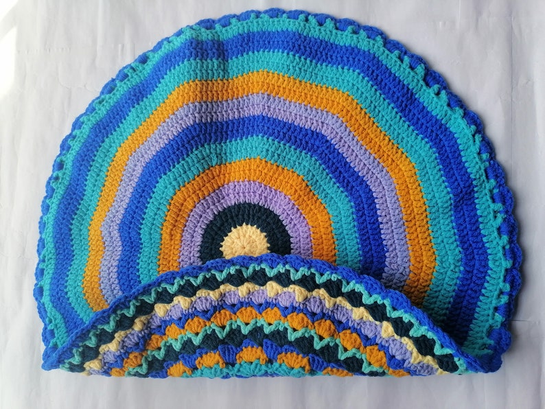 May include: A colorful crocheted round rug with a multi-colored striped pattern in shades of blue, teal, purple, yellow, and orange. The rug has a scalloped edge.