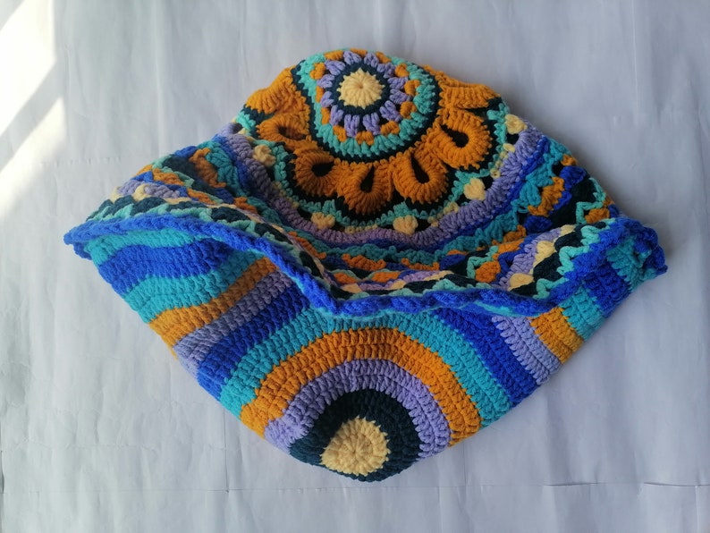 May include: A colorful crocheted blanket with a circular design in shades of blue, orange, yellow, and purple.