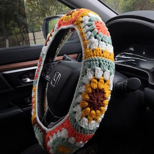 May include: A crocheted steering wheel cover with a colorful granny square pattern in shades of orange, yellow, green, white, and brown.