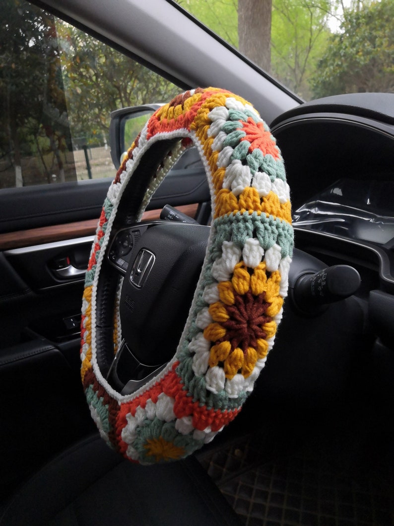 May include: A crocheted steering wheel cover with a colorful granny square pattern in shades of orange, yellow, green, white, and brown.