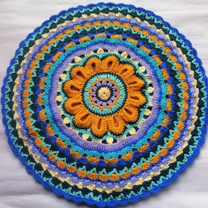 May include: A colorful crocheted mandala rug with a blue, yellow, orange, and purple design. The rug has a circular shape and a detailed pattern.