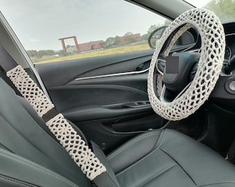 May include: White crocheted steering wheel cover and seatbelt cover for a car interior.