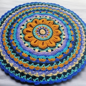 May include: A round crocheted rug with a colorful mandala design in shades of blue, yellow, and purple. The rug has a scalloped edge and is made with a variety of stitches.