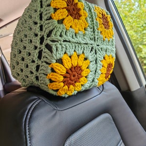 Puede incluir: Un reposacabezas de asiento de coche de ganchillo con forma de girasol. El reposacabezas est&aacute; hecho de hilo verde con girasoles de ganchillo amarillos y marrones.