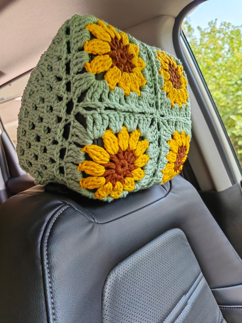 Puede incluir: Un reposacabezas de asiento de coche de ganchillo con forma de girasol. El reposacabezas est&aacute; hecho de hilo verde con girasoles de ganchillo amarillos y marrones.