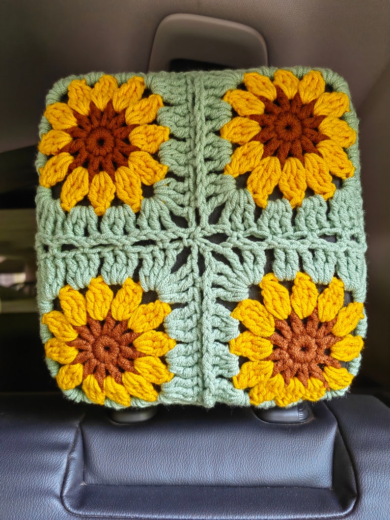 Puede incluir: Una funda para reposacabezas de asiento de coche de ganchillo con fondo verde y cuatro girasoles amarillos con centros marrones.