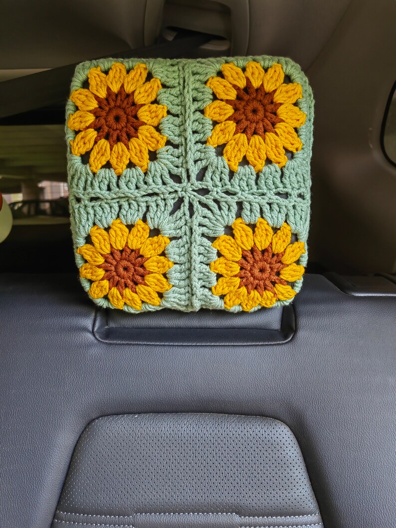 Puede incluir: Un reposacabezas de coche de ganchillo con forma de girasol. El reposacabezas est&aacute; hecho de hilo verde y amarillo y presenta cuatro girasoles de ganchillo.