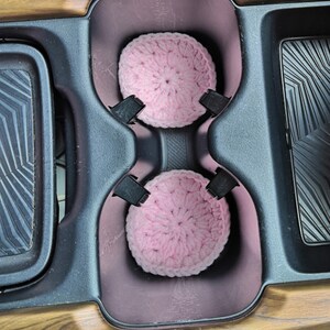 Puede incluir: Dos posavasos de ganchillo de color rosa en el portavasos de un coche.