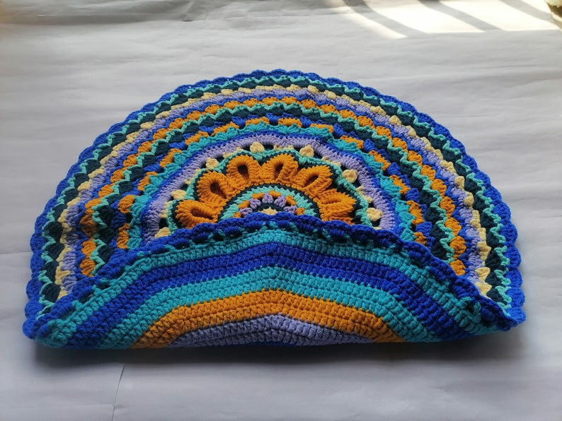 May include: A crocheted half-circle rug with a colorful mandala design in shades of blue, yellow, green, and purple.