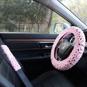 Puede incluir: Funda de volante y cintur&oacute;n de seguridad de ganchillo rosa para un coche. La funda del volante es un dise&ntilde;o grueso de ganchillo con un tejido abierto grande. La funda del cintur&oacute;n de seguridad es un dise&ntilde;o de ganchillo m&aacute;s peque&ntilde;o con un tejido m&aacute;s delicado.