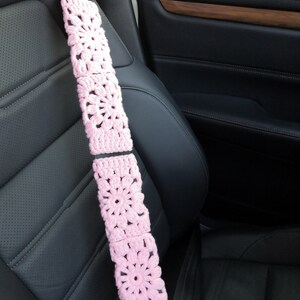 Puede incluir: Funda de cintur&oacute;n de seguridad de crochet rosa con un dise&ntilde;o floral. La funda est&aacute; hecha de varios cuadrados con una flor en el centro de cada cuadrado.