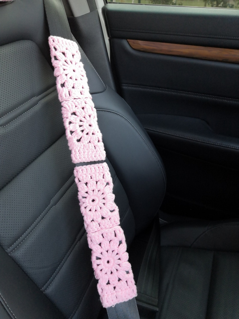 Puede incluir: Funda de cintur&oacute;n de seguridad de crochet rosa con un dise&ntilde;o floral. La funda est&aacute; hecha de varios cuadrados con una flor en el centro de cada cuadrado.