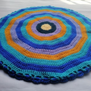 May include: A round crocheted rug with a multi-colored concentric circle pattern. The rug is made with blue, teal, orange, and purple yarn.