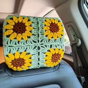 Puede incluir: Un reposacabezas de coche de ganchillo con forma de girasol. El reposacabezas est&aacute; hecho de hilo verde y marr&oacute;n y presenta cuatro grandes girasoles.