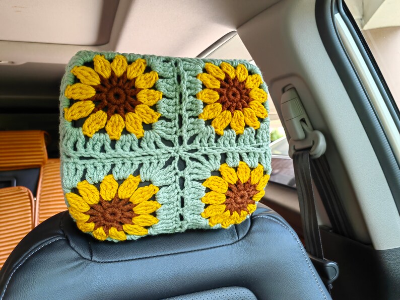 Puede incluir: Un reposacabezas de coche de ganchillo con forma de girasol. El reposacabezas est&aacute; hecho de hilo verde y marr&oacute;n y presenta cuatro grandes girasoles.