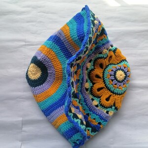 May include: A crocheted hat with a colorful circular pattern in shades of blue, purple, yellow, and orange. The hat is folded in half, revealing the intricate design.