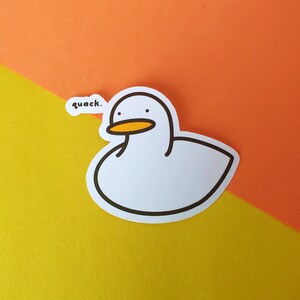 May include: White duck sticker with a yellow beak and the word "quack." on a yellow and orange background.