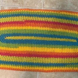May include: A colorful crocheted oval rug with stripes of orange, yellow, green, blue, and red.