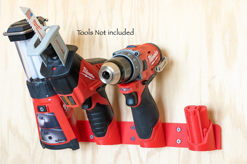 K&ouml;nnte beinhalten: Roter Werkzeughalter an einer Holzoberfl&auml;che, zur Aufnahme einer S&auml;bels&auml;ge, eines Bohrers und eines Akkus. Der Text "Tools Not included" ist sichtbar. Der Halter wird mit Schrauben befestigt.