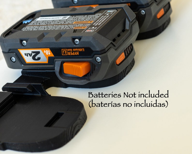 Puede incluir: Bater&iacute;as Hyper Lithium Ion de 18V negras y naranjas con una capacidad de 2Ah. Los paquetes est&aacute;n sujetos a un soporte negro. El texto "Batteries Not included" es visible.