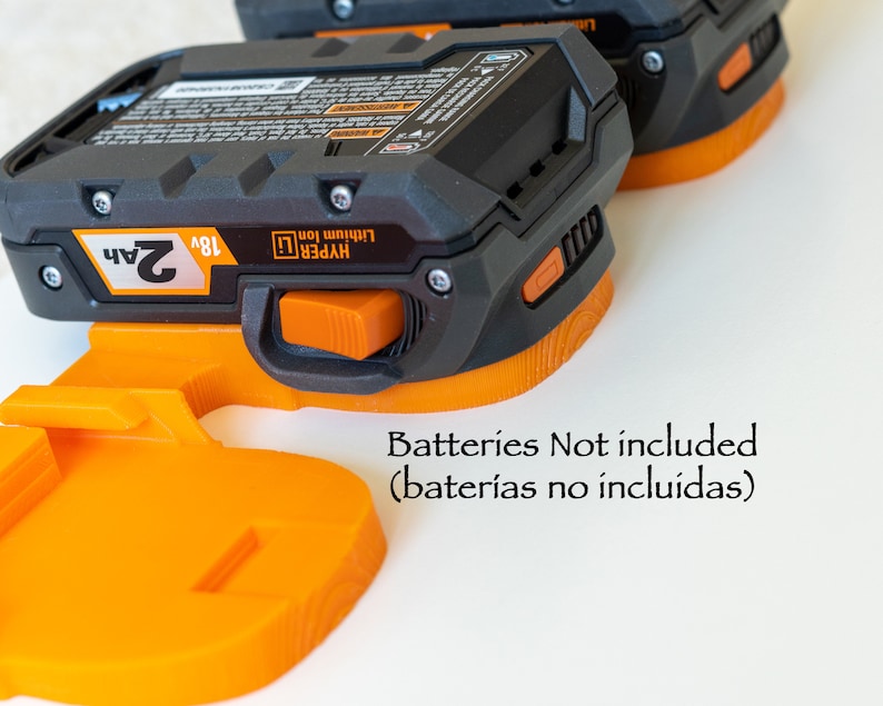 Puede incluir: Dos adaptadores de bater&iacute;a Hyper Lithium Ion de 18V en negro y naranja. Los adaptadores tienen un bot&oacute;n de liberaci&oacute;n naranja y est&aacute;n dise&ntilde;ados para bater&iacute;as de 2Ah. El texto "Batteries Not included" es visible.