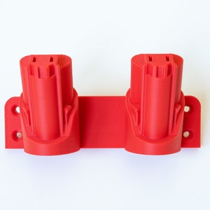 K&ouml;nnte beinhalten: Ein roter, 3D-gedruckter Werkzeug-Akkuhalter. Der Halter hat zwei zylindrische Schlitze f&uuml;r Batterien und eine rechteckige Basis mit Befestigungsl&ouml;chern. Das Design ist einfach und funktional.