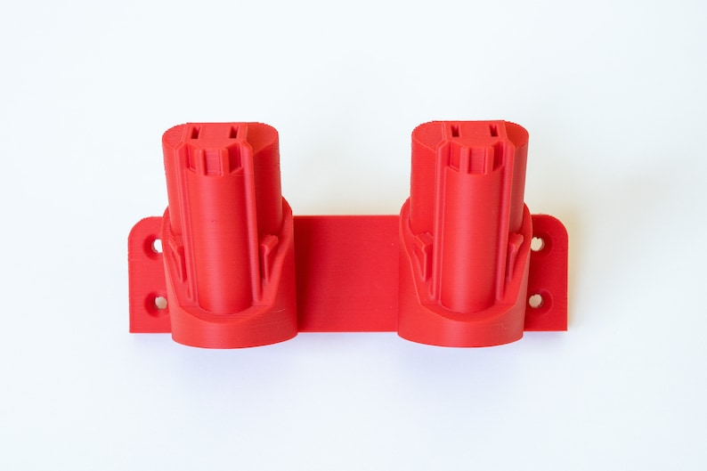 K&ouml;nnte beinhalten: Ein roter, 3D-gedruckter Werkzeug-Akkuhalter. Der Halter hat zwei zylindrische Schlitze f&uuml;r Batterien und eine rechteckige Basis mit Befestigungsl&ouml;chern. Das Design ist einfach und funktional.