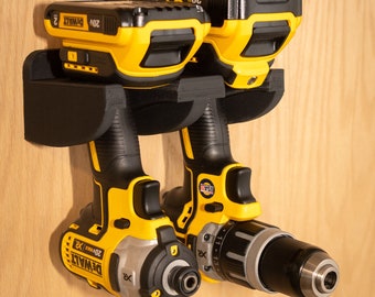 Könnte beinhalten: Schwarzer, 3D-gedruckter Bohrerhalter zur Aufnahme von zwei DeWalt 20V XR Werkzeugen. Der Halter ist auf einer Holzoberfläche montiert. Der Text "Tools Not Included" ist sichtbar.