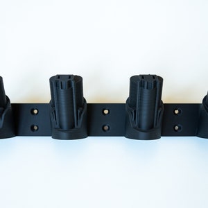 K&ouml;nnte beinhalten: Ein schwarzer, an der Wand montierter Batteriehalter mit vier Schlitzen. Jeder Schlitz ist zur Aufnahme einer Batterie konzipiert. Der Halter hat vorgebohrte L&ouml;cher f&uuml;r die einfache Installation. Er besteht aus einem haltbaren Material.